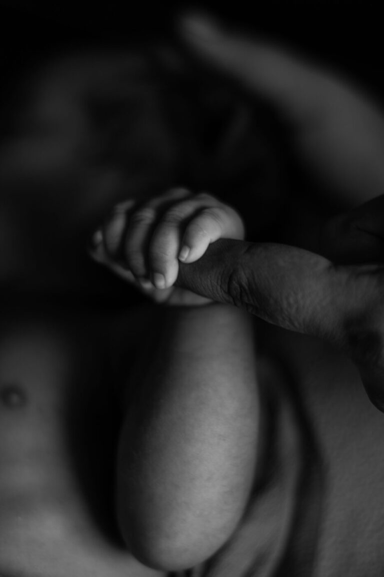 Mãozinha de recém-nascido segurando o dedo do adulto em contato pele a pele