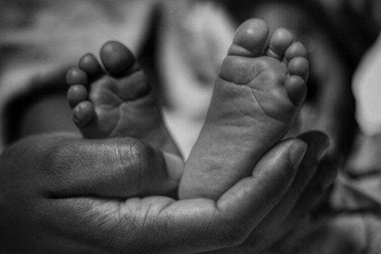 Pezinhos de recém-nascido apoiados nas mãos de um adulto