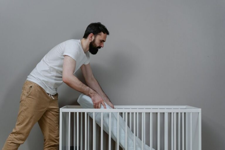 Homem barbudo montando um berço em quarto de bebê minimalista